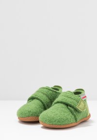 Zielone filcowe kapcie o miękkiej fakturze, z zapięciem na rzep i kauczukową podeszwą. Uzupełnione o małą czerwoną metkę po bokach.