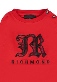 T-shirt rosso a maniche corte con logo 'JR' ricamato in nero e a motivi sopra il testo 'RICHMOND'. Collo rotondo con dettagli a bottoni.
