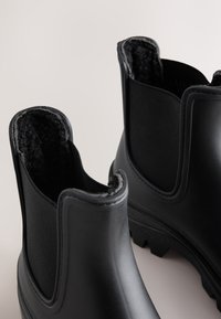 Pair of black rubber ankle boots with elastic side panels and soft, fuzzy inner lining visible.