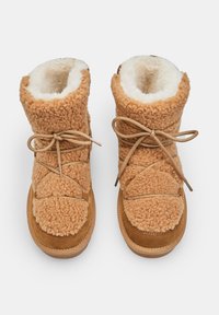 Stivali foderati in pelliccia color beige con una morbida texture pelosa, dotati di punta rotonda, design con lacci e suola di colore beige in contrasto.