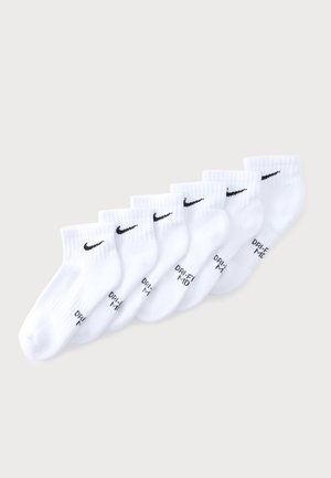 Sept paires de chaussettes de cheville Nike blanches avec logos swoosh noirs et texte "DRI-FIT", disposées en rangée diagonale sur un fond clair.