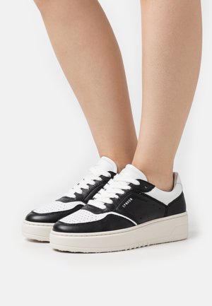 Svartvita lädersneakers med perforerad tå, vadderad tung och strukturerade sidor. Klumpig krämfärgad mellansula och vita skosnören.