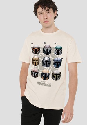 Young man wearing a light beige T-shirt with nine Mandalorian helmets arranged in a grid and "Star Wars The Mandalorian" text below.