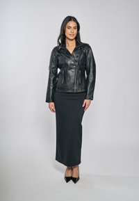 Černá kožená motocyklová bunda s přiléhavým střihem, zipovými kapsami a širokými klopami, kombinovaná s tmavou dlouhou sukní a černými podpatky.