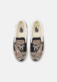 Chaussures Vans slip-on avec un grand serpent à sonnette enroulé et un motif à carreaux sur une toile noire.