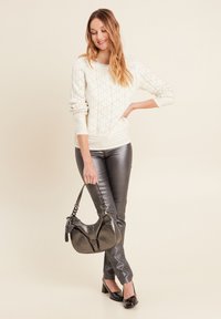 Maglione cremoso a maglia con motivo a diamante, abbinato a pantaloni grigi metallizzati attillati e una borsa nera curva con tracolla testurizzata.