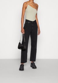 Jeans neri a vita alta con taglio dritto, abbinati a un top smanicato a coste grigio chiaro. Una piccola borsa nera con tracolla in catena argentata.