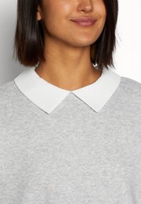 Pull gris avec un col blanc. Le tissu a une texture douce, et le col présente un design rond et plat. Aucun motif ni accent visible.