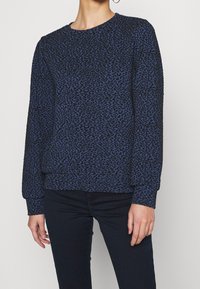 Blauwe sweatshirt met luipaardprint, een gestructureerde stof, lange mouwen, ronde hals en een losse pasvorm, gecombineerd met een donkere spijkerbroek.