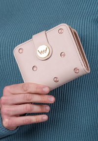 Light pink wallet with gold hardware, featuring decorative cutouts and a snap closure. Material appears textured, with a compact rectangular shape.
