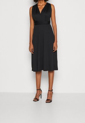 Černé šaty bez rukávů s výstřihem do V, vyztuženým pasem a sukní áčkového střihu, vyrobené z hladké látky. Kombinované s černými sandály na podpatku se širokými pásky.
