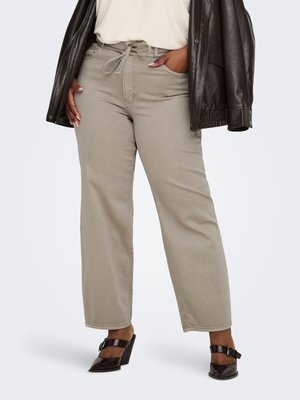 Personne portant un pantalon beige à cordon, un haut blanc, une veste en cuir marron foncé et des chaussures à talons marron foncé avec boucles.