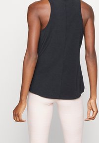 Top negro sin mangas hecho de una tela suave, con cuello redondo y dobladillo curvado. Combinado con leggings de color rosa claro con un patrón a cuadros.