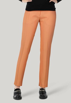 Orange tailored pants with a smooth texture and slim fit. Features side pockets and a crease down the front. Paired with black loafers.