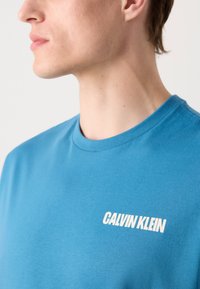 T-shirt in cotone blu con collo rotondo, con logo bianco "CALVIN KLEIN" sul lato sinistro del petto. Texture liscia, vestibilità casual, design minimal.