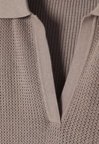 Krémový pletený svetr s výstřihem do V, s texturovaným ribováním a otevřeným pletením. Měkká látka s volným střihem a jemným leskem.