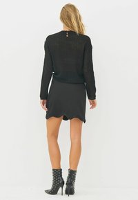 Black knitted sweater with textured sleeves, paired with a black mini skirt featuring a scalloped hem. Worn with studded black ankle boots.
