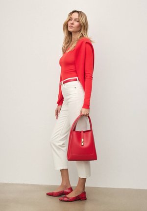 Sac à main en cuir rouge avec une forme structurée, ferrures dorées, associé à un haut rouge ajusté, un pantalon blanc raccourci et des ballerines rouges à motif.
