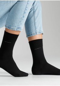Črne gležnjarice iz mehkega materiala, z rebrastim zgornjim robom in majhno oznako s tiskom "CA-SOFT" v sivi barvi.