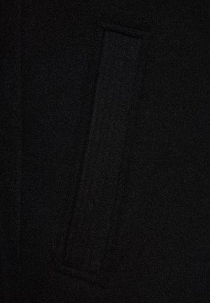 Czarna wełniana tkanina płaszcza z widoczną prostokątną kieszenią klapową i subtelnymi detalami szycia.