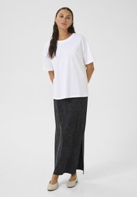 T-shirt en coton blanc avec un petit motif en forme de cœur sur la poitrine, associé à une longue jupe grise foncé dotée d'une fente sur le côté et d'une texture douce.