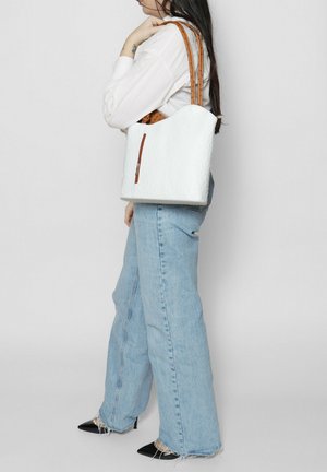 Witte texture tote bag met bruine leren handvatten en een ritsaccent. Casual gedragen met lichtblauwe wijde jeans en zwarte puntige schoenen.