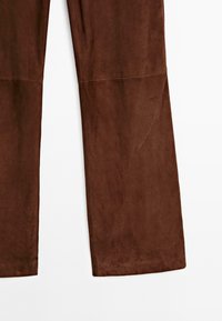 Brązowe zamszowe spodnie o gładkiej fakturze, szerokich nogawkach i prostym fasonie. Posiadają delikatne szwy i naturalny luźny krój.