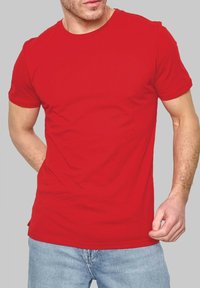T-shirt en coton rouge avec un col rond et des manches courtes, arborant un design simple et une silhouette ajustée, associé à un jean bleu.
