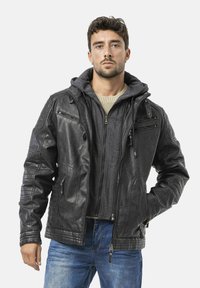 Zwarte leren jas met doorgestikte schouderdetails, meerdere ritssluitingen, gedragen over een grijze hoodie. Voorzien van zilverkleurige hardware accenten.