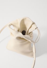 Borsa a tracolla in pelle crema con una finitura morbida e testurizzata. Presenta una forma arrotondata, una tracolla regolabile e un'apertura arricciata nella parte superiore.