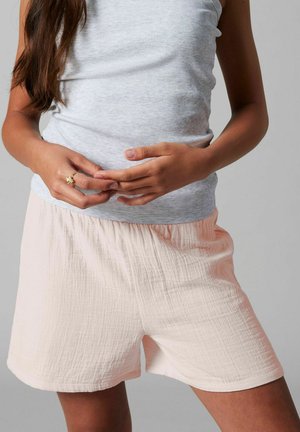 Femme portant un débardeur côtelé gris clair et un short ample texturé rose pâle, les mains jointes à la taille.