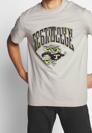 Camiseta de algodón gris claro con un gráfico en negro y verde neón que presenta una figura estilizada y texto en negrita en diseño en arco. Mangas cortas.