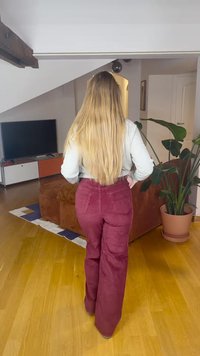 Široke hlače iz bordo korduroja z zadnjimi žepi, kombinirane s svetlo obarvano majico z dolgimi rokavi, pogled od zadaj.