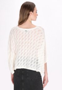 Maglione a maglia aperta color crema con una vestibilità ampia, caratterizzato da un collo ampio e maniche ¾. Il motivo ricorda le foglie, mettendo in mostra una texture morbida.