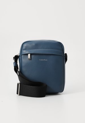 Blaue Leder-Crossbody-Tasche mit strukturierter Oberfläche, ausgestattet mit einer vorderen Reißverschlusstasche, einem silbernen Logo und einem verstellbaren schwarzen Tragegurt.
