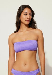 Fioletowy bikini top w stylu bandeau z teksturowanym falistym wzorem i gładkim wykończeniem. Pasujące bikini dno ma podobny design i kolor.
