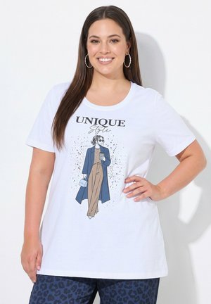 Smiling woman with straight brown hair wears white T-shirt with fashion illustration and text "Unique Style" and blue patterned pants.