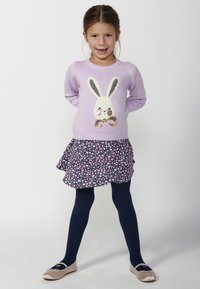Helles lila Sweatshirt mit einem Hasenmotiv, kombiniert mit einem ausgestellten marineblauen Rock mit floralen Mustern. Marineblaue Strumpfhosen und beiger Ballerinas runden das Outfit ab.