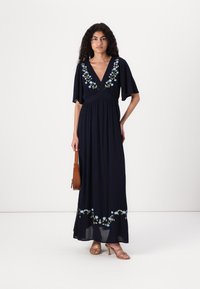 Navy maxi dress with elbow-length sleeves, deep V-neck, and floral embroidery in blue and green. Smooth fabric and flared hemline.