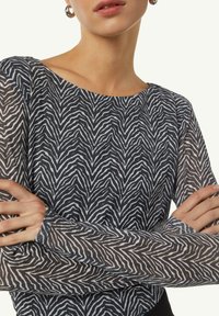 Langärmliges Oberteil mit einem schwarz-weißen Zickzackmuster auf transparenter Materialien, runder Halslinie und taillierter Form.