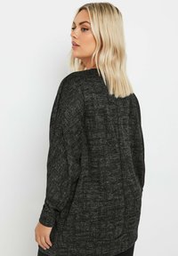 Czarna, teksturowana tunika z długimi rękawami, o luźnym kroju i subtelnym wzorze. Tył ma centralny detal szwu.