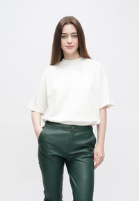 Roomkleurig oversized t-shirt met een ronde hals, gecombineerd met nauwsluitende donkergroene leren broek met een sluiting met knopen aan de voorkant.