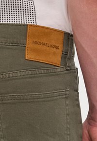 Olive színű nadrág texturált anyagból, hátulján "MICHAEL KORS" felirattal bélelt, világosbarna velúr címkével.