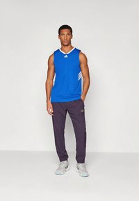 Mėlyni rankovių atletinio stiliaus marškinėliai su baltais akcentais, derinami su tamsiai purpurinėmis sportinėmis kelnėmis ir pilkais sportiniais batais su mėlynais pado akcentais.