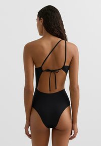 Čierny jednodielny plavky s vysokým vykrojením na nohách, otvorenými chrbtom, úzkymi nastaviteľnými ramienkami a zapínaním na mašľu. Hladká textúra materiálu.