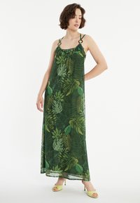Maxikleid in Grün mit Blattdruck, dünnen Trägern mit runder Hardware und lockerer Passform, die bis zu den Knöcheln fällt.