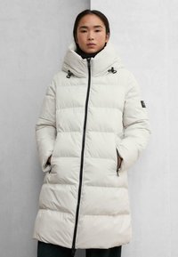 Piumino chiaro con trapuntatura orizzontale, collo alto e dettagli in metallo nero. Presenta tasche con zip e una silhouette rilassata.