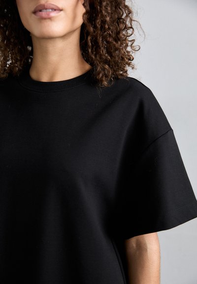 Fekete, rövid ujjú pamut póló kerek nyakkal, laza fazonnal és sima textúrával. Nincsenek látható minták vagy fém típúsú részletek.