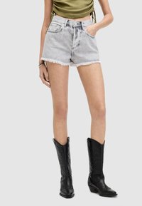 Shorts de mezclilla en un lavado claro con dobladillo deshilachado, combinados con altas botas de vaquero negras con detalles en relieve.