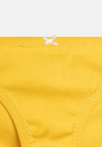 Rumene bombažne spodnje hlačke z gladko teksturo, ki imajo nežno valovito rob in majhno belo okrasno pentljo na pasu.